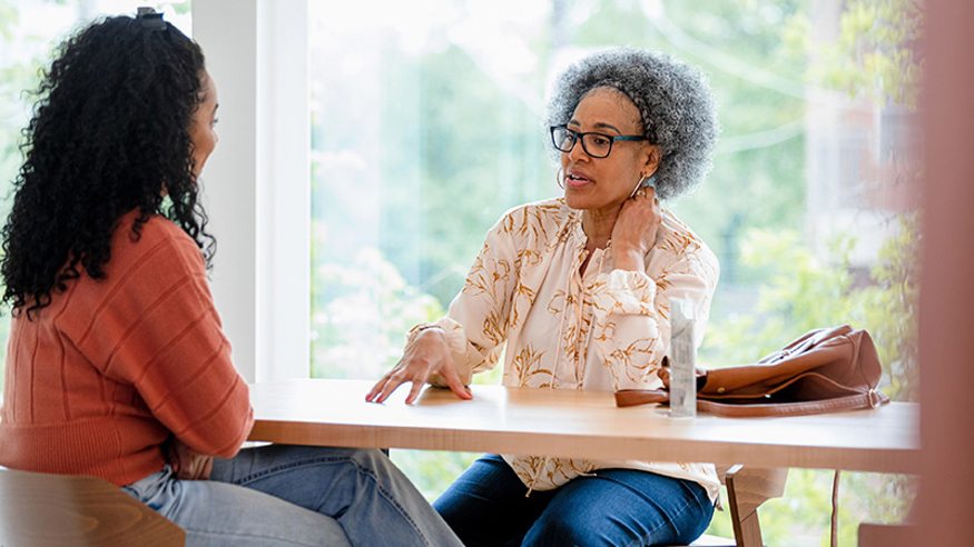 Sharing your diagnosis with a loved one. Mother and daughter sitting across from each other at a table. Mother is talking.